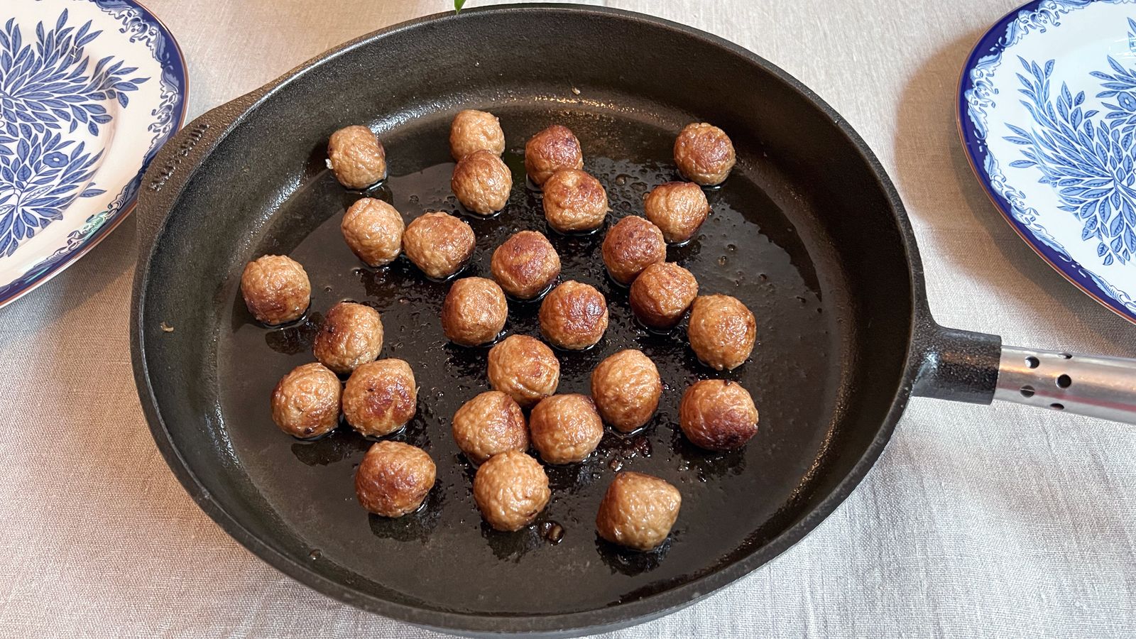 Gjutjärnspanna med stekta köttbullar på ett dukat bord.